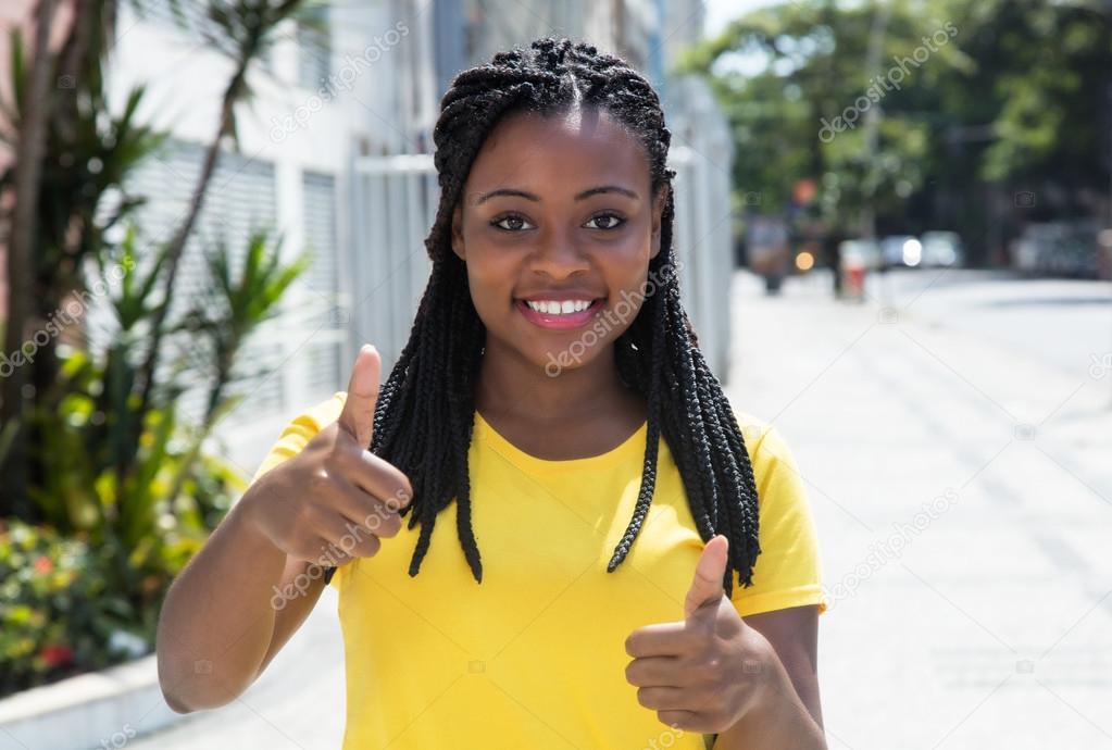 African american woman in a yellow shirt in city showing thumb