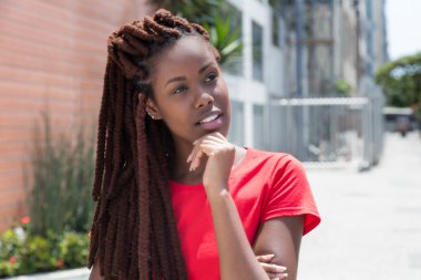 Thinking african woman with dreadlocks in the city clipart