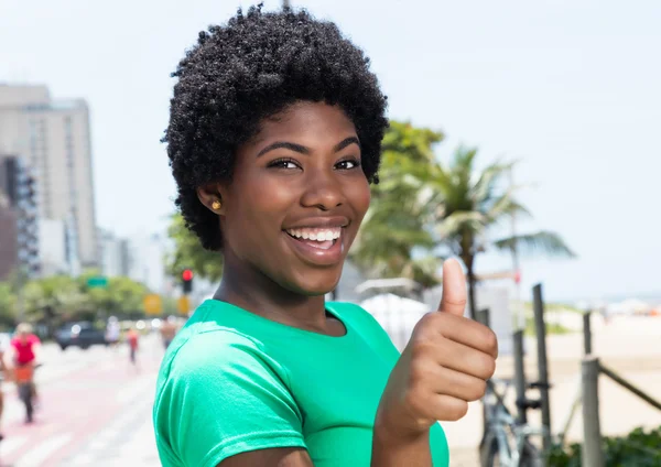 Mulher africana em uma camisa verde na cidade mostrando polegar — Fotografia de Stock