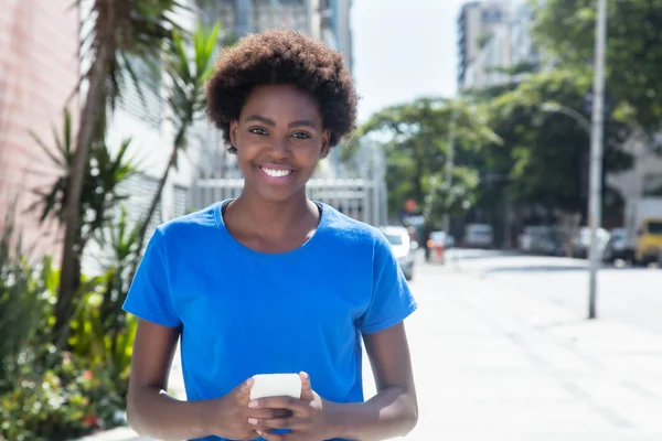 Rindo mulher afro-americana em uma camisa azul datilografando mensagem — Fotografia de Stock