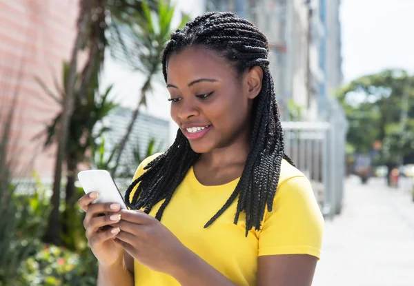 African american woman in a yellow shirt texting message with mo — Stock Photo, Image