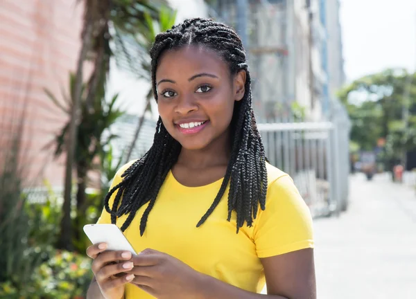 African american woman in a yellow shirt typing message with mob — Stock Photo, Image