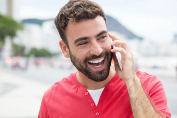 Gelukkig man met rode shirt op de mobiele telefoon in de stad — Stockfoto