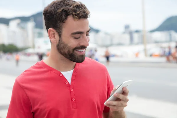 Man with red shirt sending message with phone in the city — Stock Photo, Image