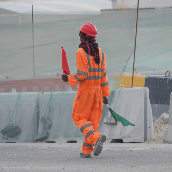 A construction worker with green and red flag guiding the excavator driver.