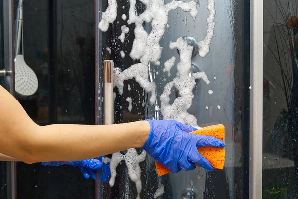 Cleaning of shower steam cabins from calcium deposits. Cleaning in the bathroom. hand in gloves with rag and detergent washing shower and glass