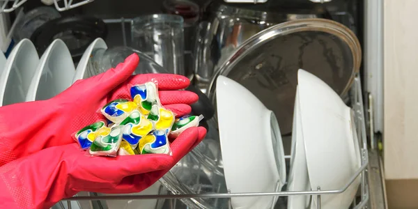 Миючі засоби для посудомийної машини в руках. руки в рожевих гольвах тримають гелеві капсули для посудомийної машини. Капсула для посудомийної машини. Блискуча чистота . — стокове фото