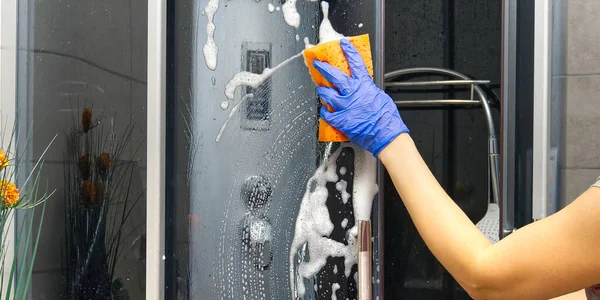 Cleaning of shower steam cabins from calcium deposits. Cleaning in the bathroom. hand in gloves with rag and detergent washing shower and glass