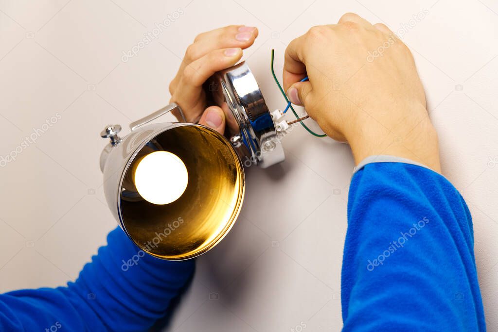 Male electrician connects the wall lamp at domestic house