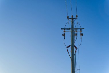 Elektrik güç gökyüzü hatları ve tahta bir direğin üzerindeki bağlantılar. Elektrik kabloları ve mavi gökyüzü kabloları. Mavi gökyüzüne karşı ahşap elektrik direği.