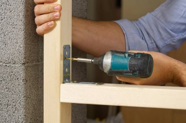 Craftman portatif bir tornavida tutuyor. Tahtaya vida vidalanmış metal vidaları tamir etmek için. DIY kavramı