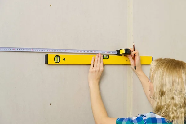 DIY blond young attractive woman using spirit level to work out measurements on plasterboard wall. DIY concept