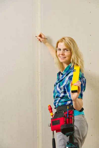 塗装されていない石膏ボードの壁の背景にツールの様々なフルDiyツールベルトを身に着けているブロンドの女性 Diy女性のコンセプト — ストック写真