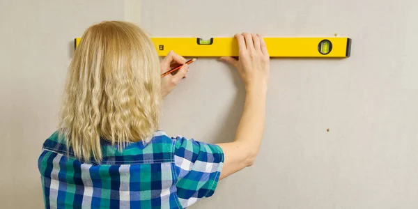 DIY blond young attractive woman using spirit level to work out measurements on plasterboard wall. DIY concept