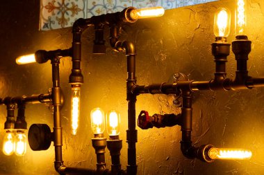 Su borularından yapılmış modern kurşun lamba. Kırsal tasarım, ampullü ve borulu sıva duvarı. inşaat atığı geri dönüşüm kavramı