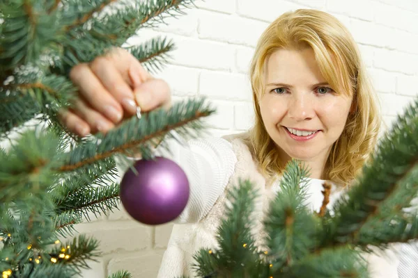 Blond jolie femme décorant arbre de Noël avec des ornements violets boules de décoration. — Photo