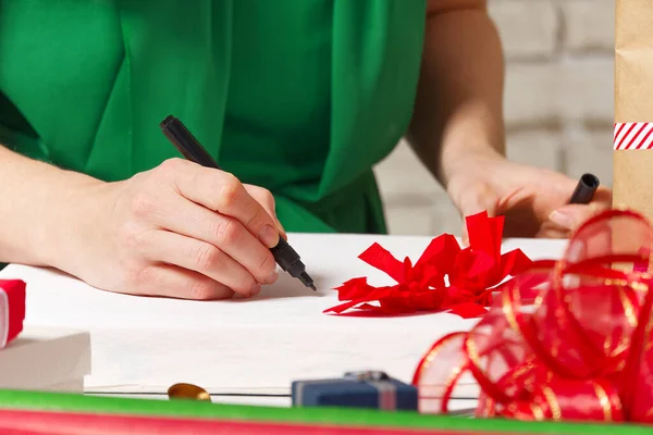 Kobieta podpisuje prezenty świąteczne czarnym długopisem. Prezenty świąteczne pakowania — Zdjęcie stockowe