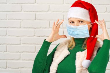 Koruyucu tıbbi maske takan ve Noel Baba şapkası takan bir kadın. Kadınlar Covid-19 Coronavirus 'u korumak için Cerrahi maske takmayı öğretiyor.