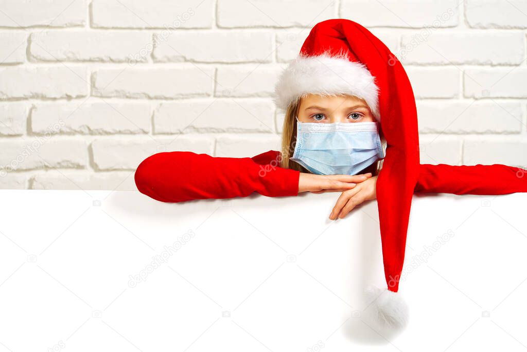 sad girl in red gnome hat and medical face mask. covid concept christmas mockup copy space. Sad child face with red santa claus hat and surgical mask.