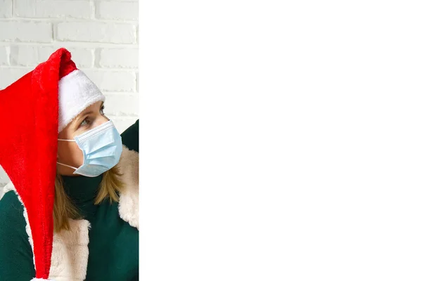 Blonde Frau mit medizinischer Gesichtsmaske, die hinter einer weißen Plakatwand hervorlugt. Wichtelmädchen, Kopierraum. Gepflegtes Weihnachtskonzept — Stockfoto