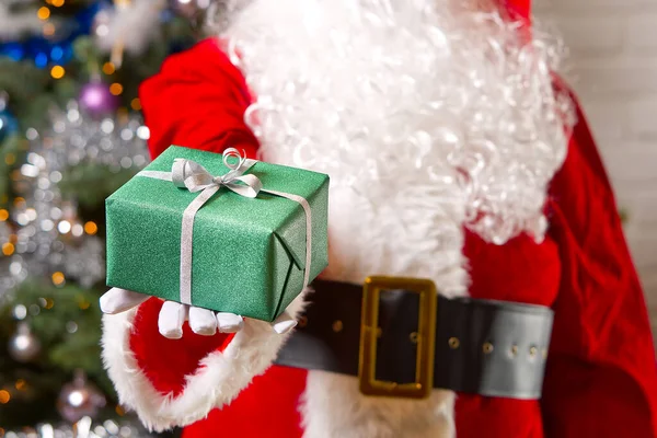 Mikulás kezét tartja zöld ajándék doboz szemben karácsonyfa. — Stock Fotó