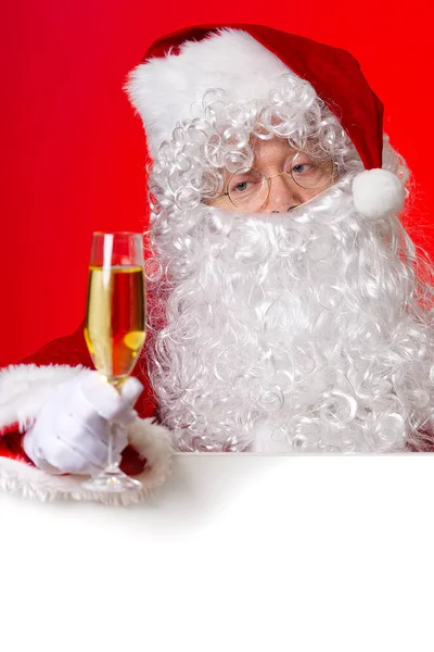 Święty Mikołaj trzymając szklankę musującego wina w ręku stojąc za pustą tablicą. przestrzeń kopiowania. — Zdjęcie stockowe
