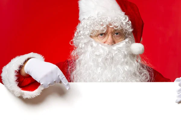 Santa Claus patrząc zza pustej tablicy białej izolowane na czerwonym tle z miejsca kopiowania — Zdjęcie stockowe