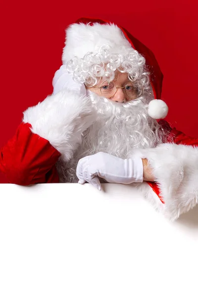 Der Weihnachtsmann schaut hinter der leeren weißen Tafel auf rotem Hintergrund mit Kopierraum hervor — Stockfoto