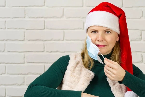 Egy piros kalapos nő orvosi maszkot visel. női télapó sapkát visel. Karácsony és újév a kovácsolt koncepcióban. — Stock Fotó