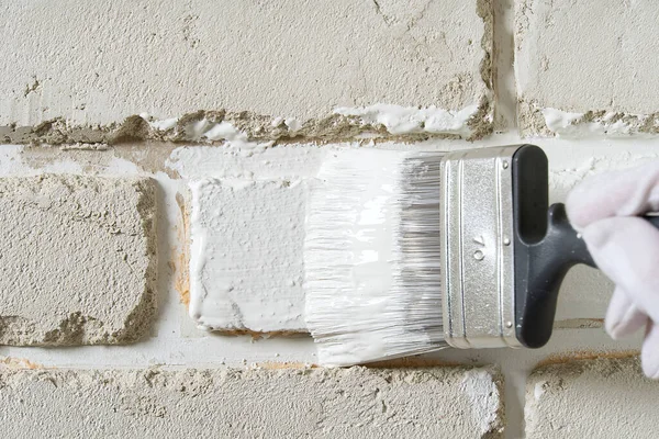 DIY wall repairing, Woman painting a white brick wall with a paint brush