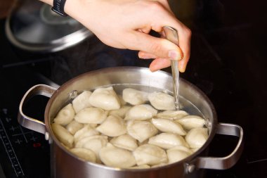 Aşçı köfteleri bir kaşık dolusu kaynar suyla karıştırıyor. Tavada haşlanmış hamur köftesi.