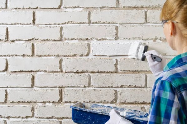 DIY wall repairing, Woman painting a white brick wall with a paint brush