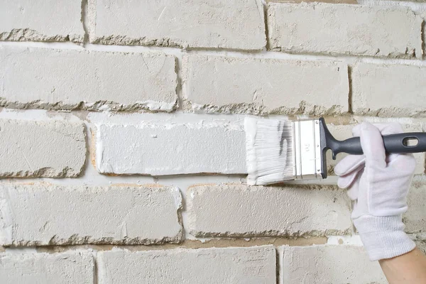 DIY wall repairing, Woman painting a white brick wall with a paint brush