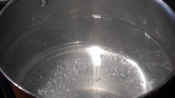 Cerrar el agua caliente hirviendo con un montón de burbujas en un quieto de una sartén gris plateado. — Vídeo de stock