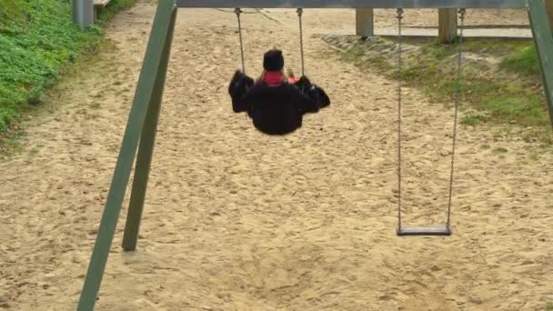 Mulher de vestido preto está balançando em um balanço sozinho no parque. — Vídeo de Stock