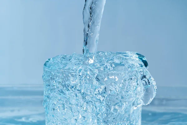 Выливание чистой питьевой воды из голубой пластиковой бутылки в стекло на голубом фоне — стоковое фото