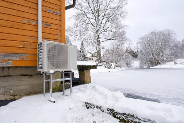 Air to water heat pump near an old wooden house in winter. air water heatpump, low emission renewable energy close up