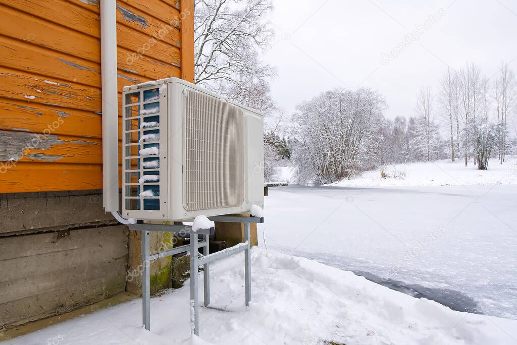 Air to water heat pump near an old wooden house in winter. air water heatpump, low emission renewable energy close up