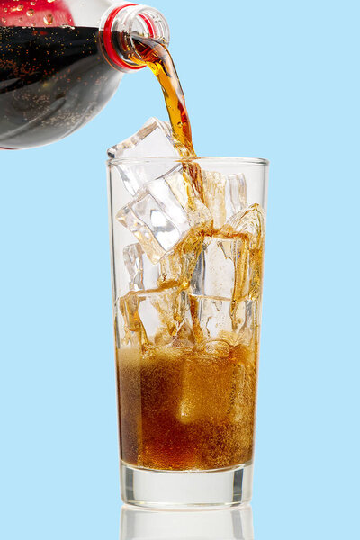 Pouring Cola to glass with ice cubes isolated on blue, copy space