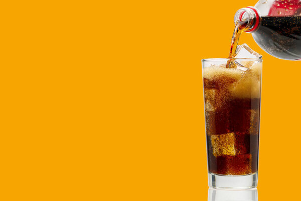 Pouring Cola to glass with ice cubes isolated on orange, copy space