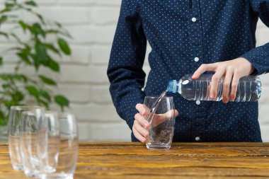Çocuk plastik şişeden ahşap masadaki cama su döküyor.
