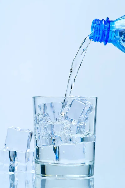 Despejando água potável limpa de garrafa de plástico azul em vidro no fundo azul — Fotografia de Stock
