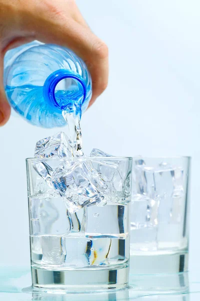 Despejando água potável limpa de garrafa de plástico azul em vidro no fundo azul — Fotografia de Stock