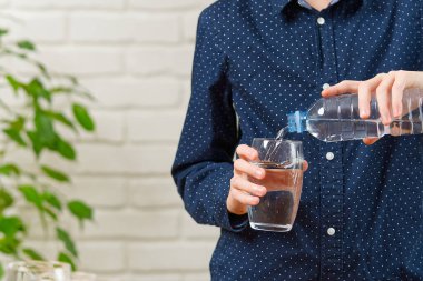 Çocuk plastik şişeden ahşap masadaki cama su döküyor.