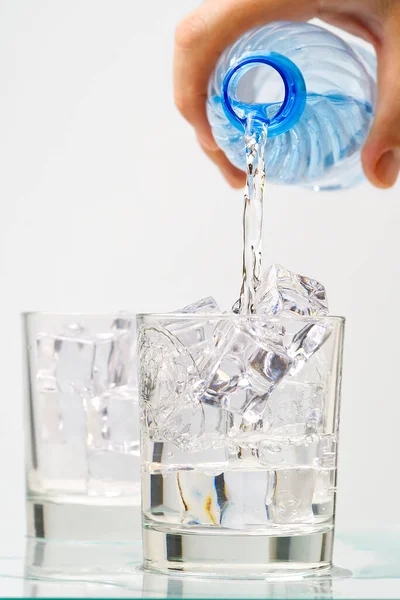 Despejando água potável limpa de garrafa de plástico azul em vidro no fundo azul — Fotografia de Stock