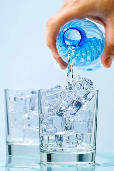 Despejando água potável limpa de garrafa de plástico azul em vidro no fundo azul — Fotografia de Stock