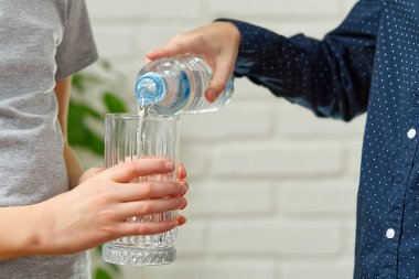 Çocuk plastik şişeden ahşap masadaki cama su döküyor.