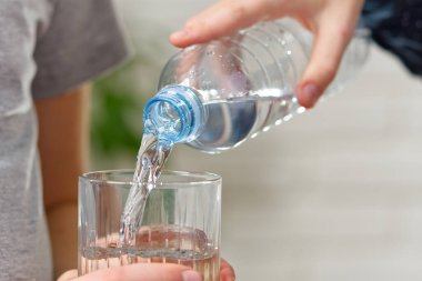 Çocuk plastik şişeden ahşap masadaki cama su döküyor.