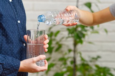 Çocuk plastik şişeden ahşap masadaki cama su döküyor.