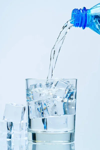 Наливання чистої питної води з блакитної пластикової пляшки в склянку на синьому фоні — стокове фото